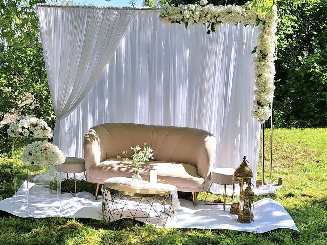 Décor de cérémonie installé en extérieur, tenture blanche et arche fleurie