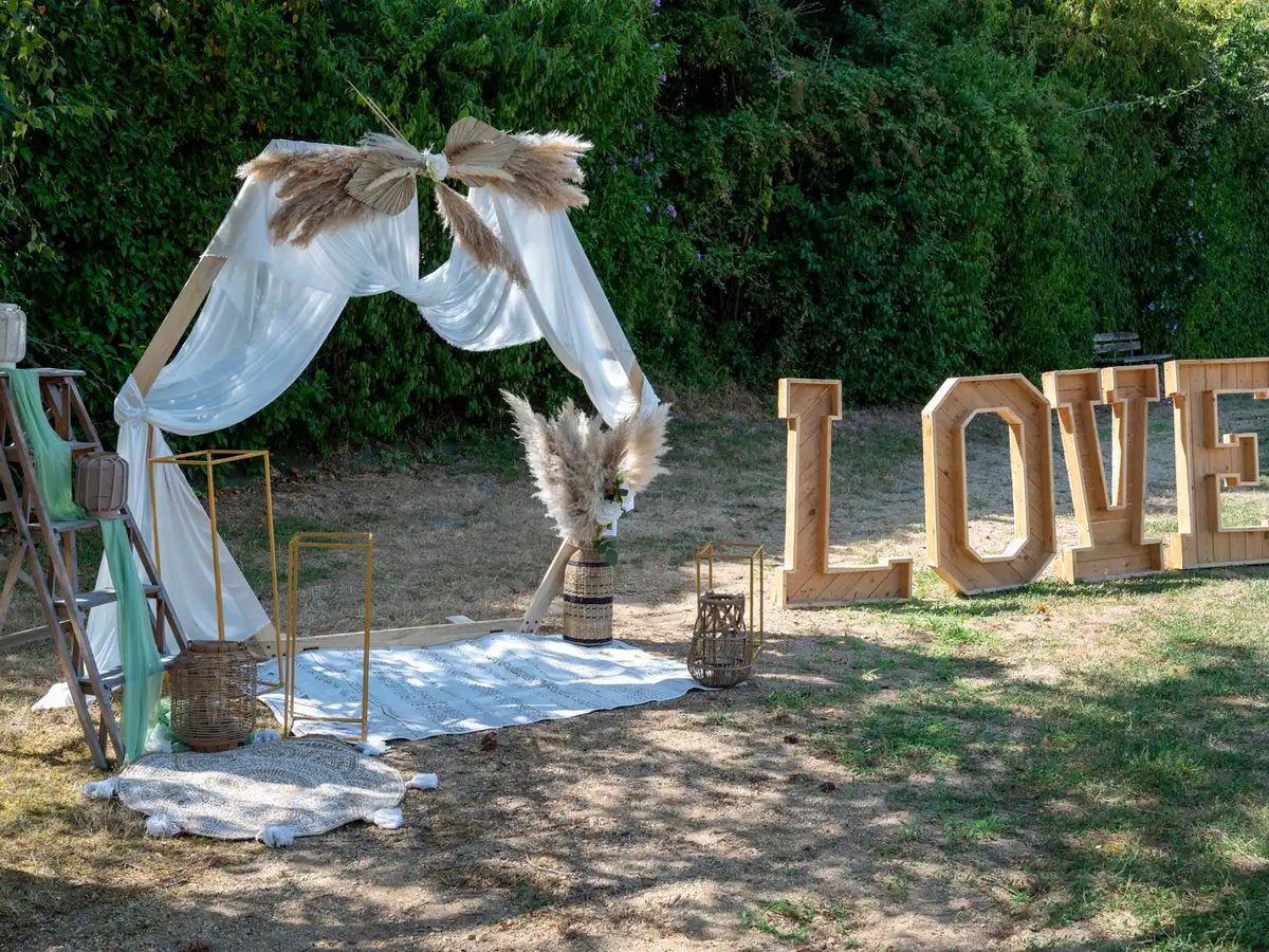 Arche de cérémonie extérieure drapée de voile blanc et lettres LOVE en bois